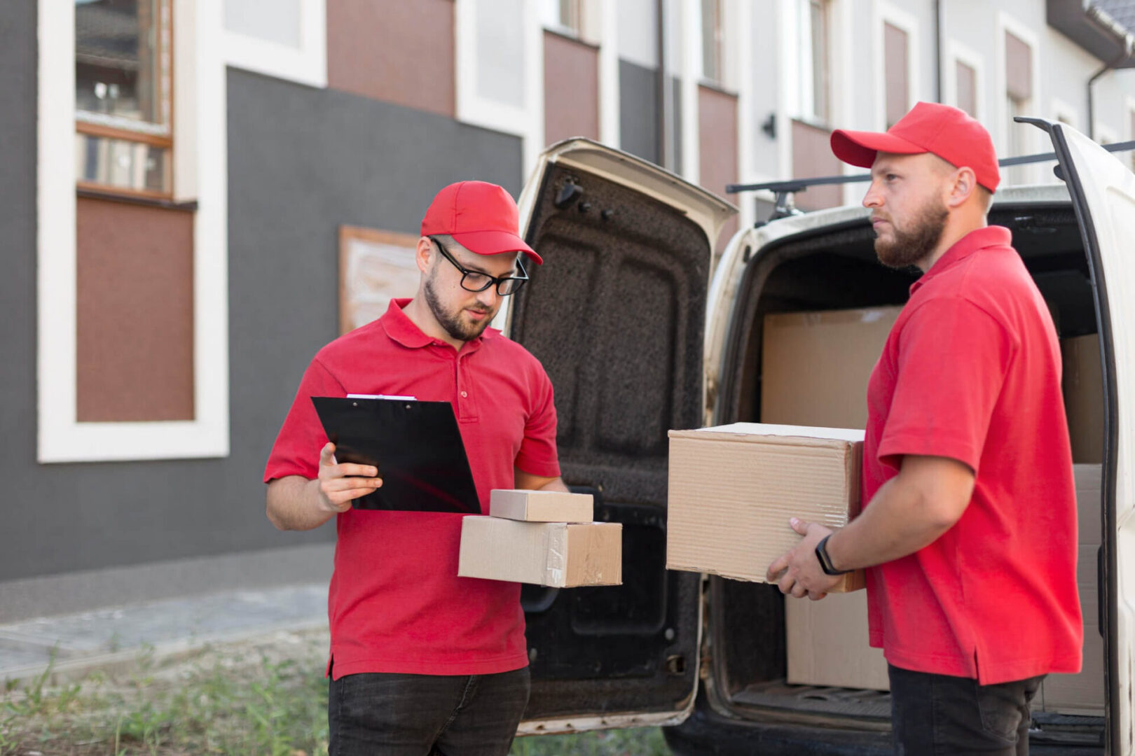 Two men in red shirts holding boxes near a van.